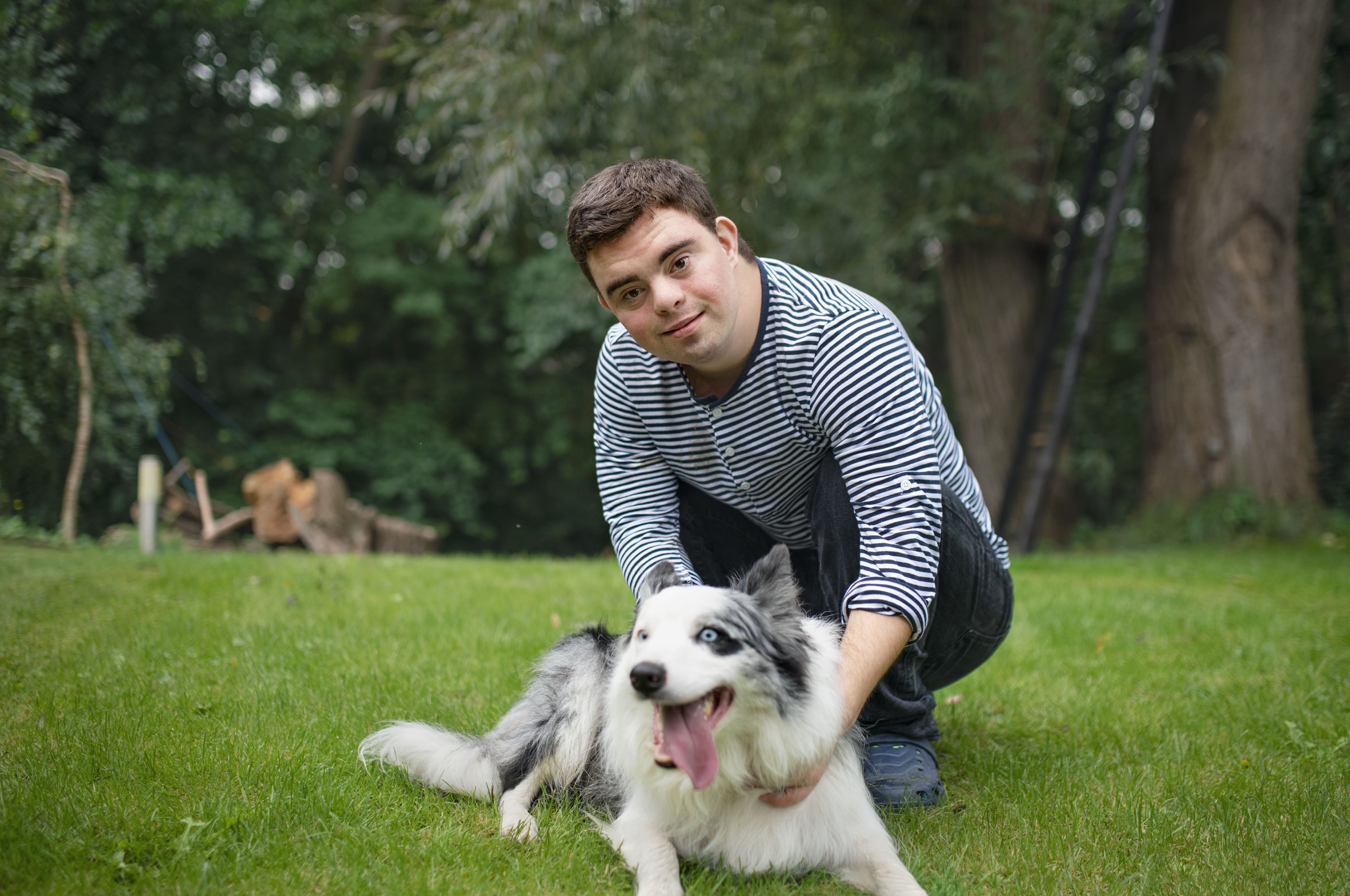 Mensch mit Down Syndrom spielt mit seinem Hund im Garten